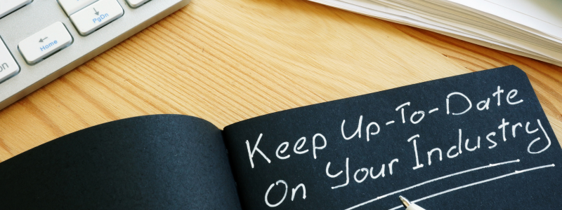 black notebook with white writing that says "keep up to date on your industry"